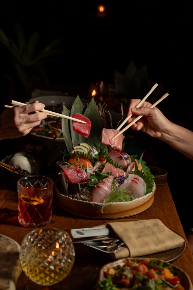 Guests picking sashimi from a shared platter with chopsticks at BABOU